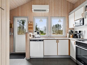 Eine moderne Küche mit Holzwänden, weißen Schränken und großen Fenstern mit Blick auf Bäume.