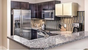 A modern kitchen with dark cabinets, stainless steel appliances, a granite countertop, and a striped backsplash.