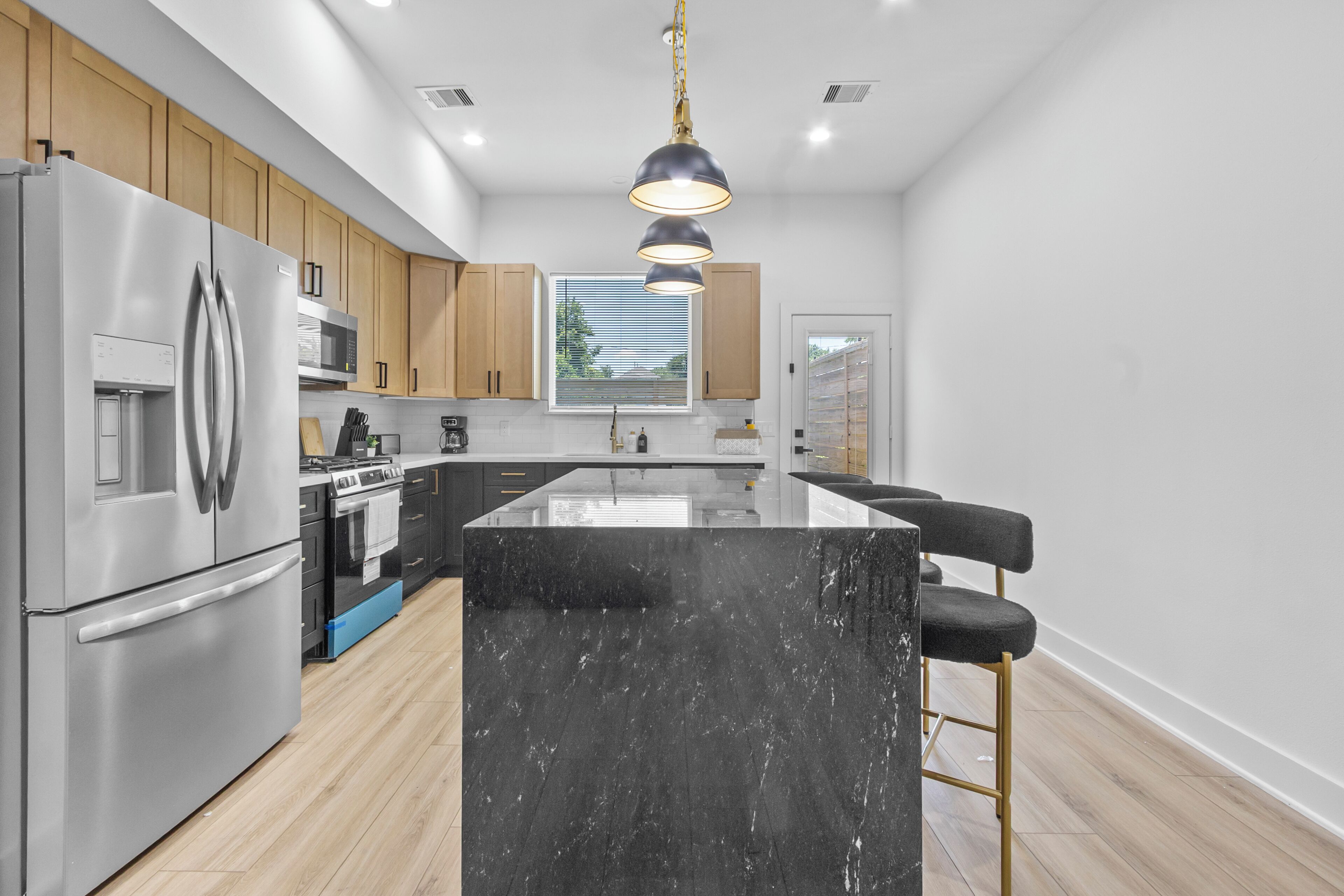 A modern kitchen with a central island, stainless steel appliances, wooden cabinets, and a pendant light.