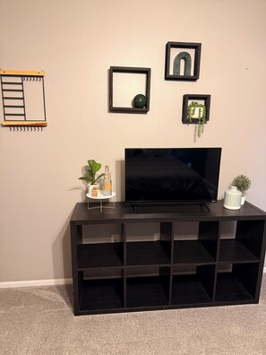 Un meuble de rangement noir pour appareils électroniques, avec un téléviseur à écran plat, une petite plante et un miroir encadré accroché au mur.