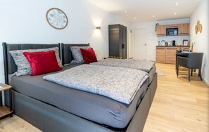 A modern bedroom with a large bed, a desk, and a kitchenette in the background. - Vacation apartment 2 - Gasthaus Bußmann (Vreden)
