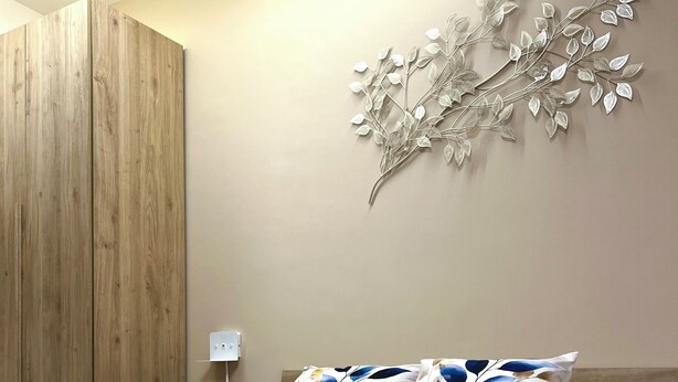 A neatly made bed with decorative pillows, a wall art piece, and a folded towel on the bed.