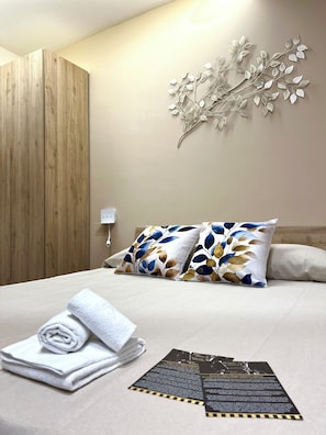 Una cama bien tendida con almohadas decorativas, una obra de arte en la pared y una toalla doblada sobre la cama.