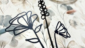 A vase with black paper flowers on a floral-patterned tablecloth.