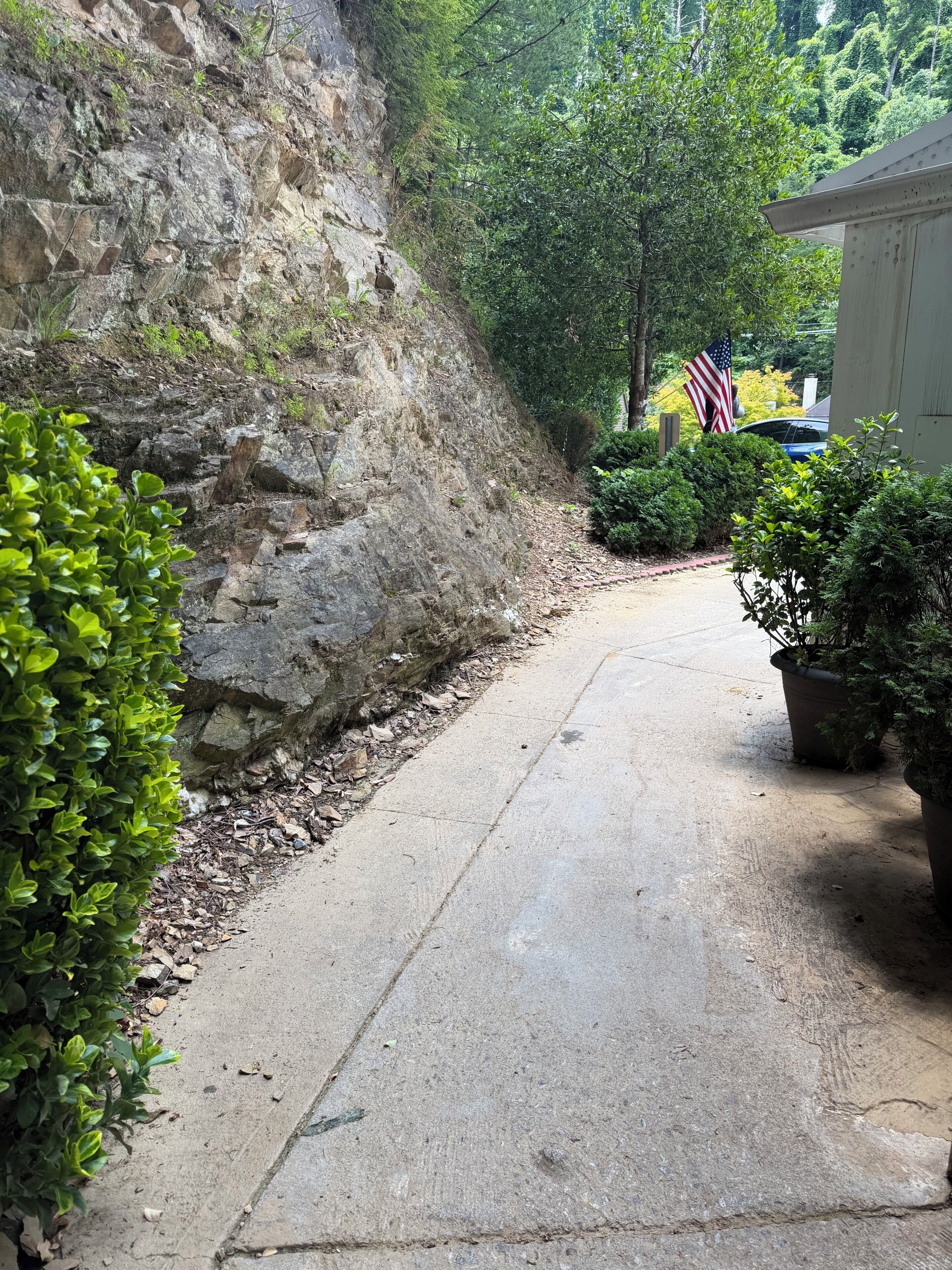 A concrete pathway flanked by greenery and a stone wall, leading to a building with an American flag.