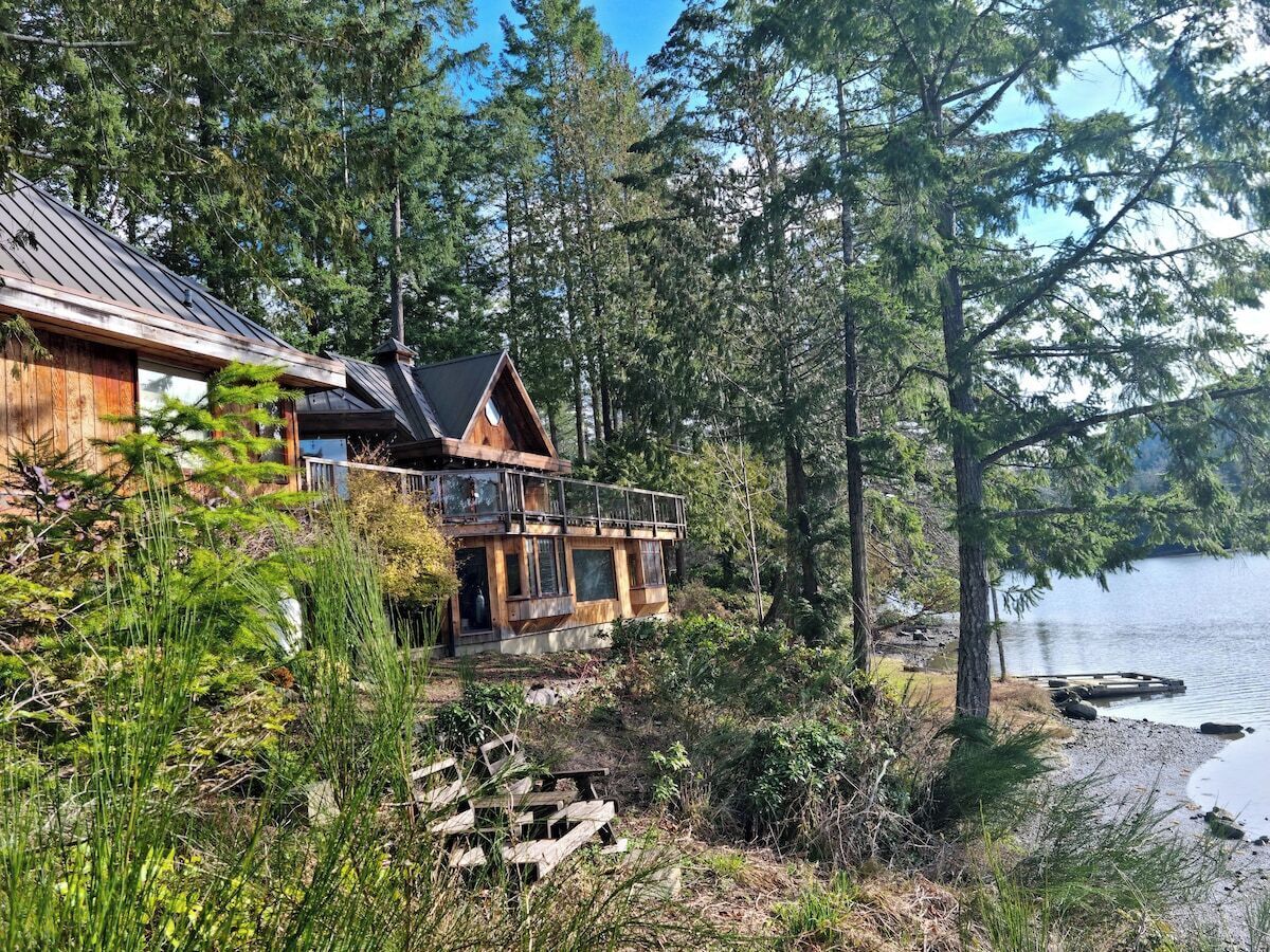 A cabin with a deck overlooking a lake, surrounded by dense forest.