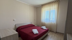 Ein Hotelzimmer mit einem Bett, einem Nachttisch, einem Fenster mit Vorhängen und einem hellen Boden.