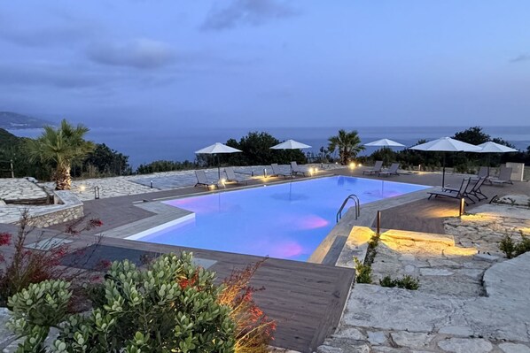 A pool with a view of the sea, surrounded by lounge chairs and umbrellas.