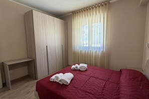 A bedroom with a bed, a wooden wardrobe, a desk, and a window with curtains. - Sea-view apartment with a pool (Telegrafo)