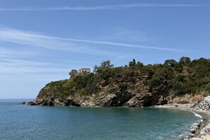 Eine Küstenlandschaft mit einem Gebäude auf einer Klippe, blauem Himmel und ruhiger See.