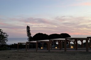 A series of wooden pergolas with seating areas, set against a backdrop of trees and a sunset sky. - Sea-view apartment with a pool (Telegrafo)