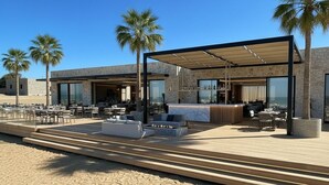 A modern outdoor dining area with a bar, seating, and palm trees. - Protels Royal Bay Resort & Spa (Hurghada)