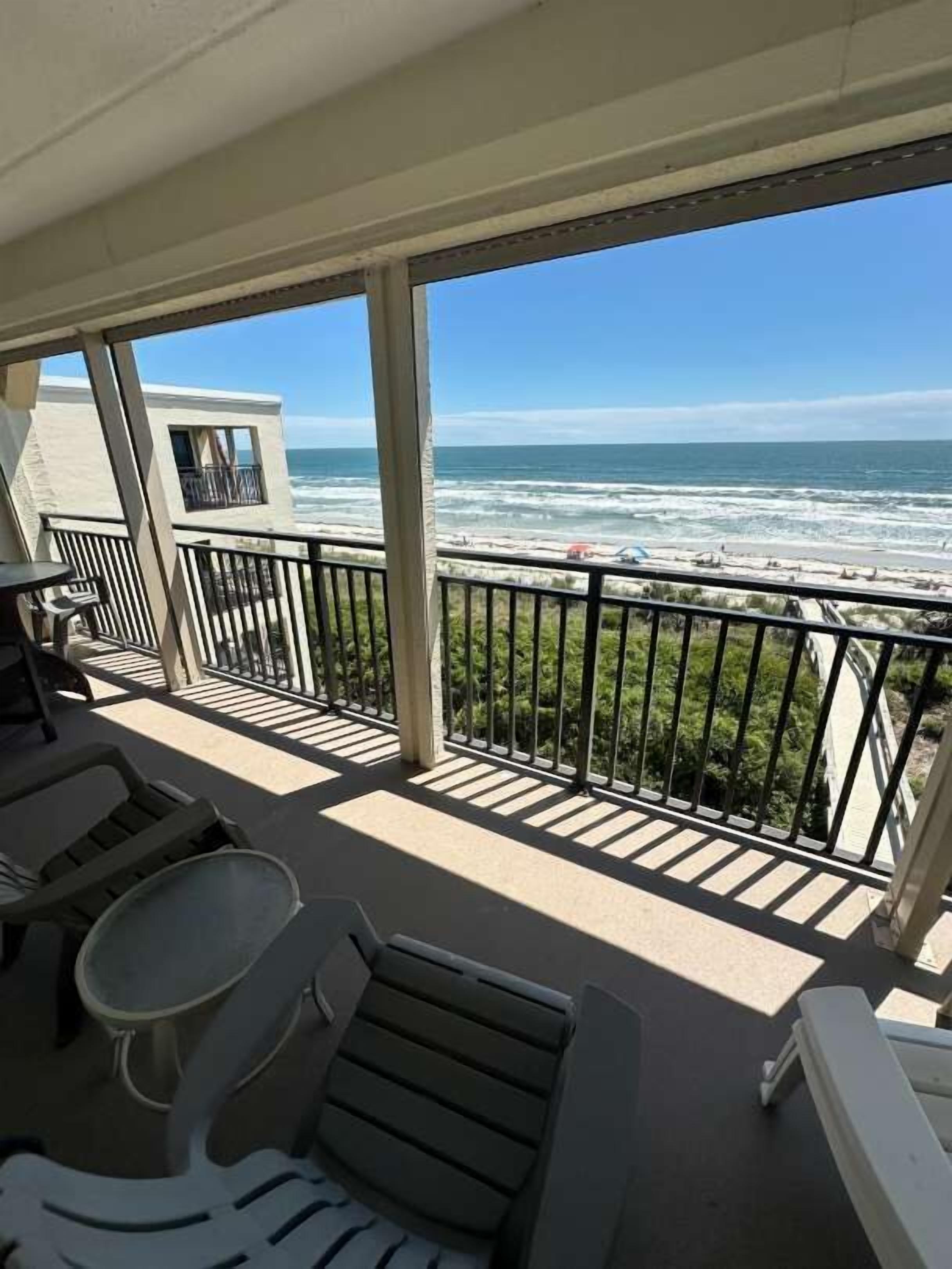 A balcony with a view of the ocean, outdoor furniture, and a building in the background.