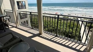 A balcony with a view of the ocean, outdoor furniture, and a building in the background. - Ocean Front Beach Condo - Windjammer 410 (St. Augustine)