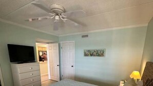 A bedroom with a bed, a ceiling fan, a television, a dresser, and a door leading to another room. - Ocean Front Beach Condo - Windjammer 410 (St. Augustine)