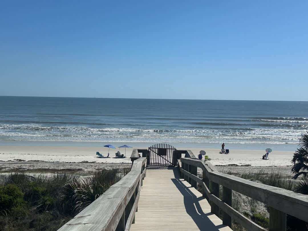 A wooden boardwalk leading to a beach with a gate, sandy beach, and ocean view.