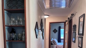 Un passadís amb sòl de fusta, una catifa amb dibuixos, una reixa metàl·lica i una porta que dona a un dormitori.