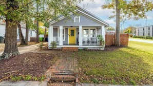 A single-story house with a front porch, a yellow door, and a brick pathway leading to the entrance. - Backyard Hangout Firepit, Giant Connect 4 & BBQ (Raleigh)