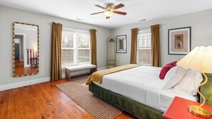 A bedroom with a bed, a ceiling fan, a window with curtains, a bedside table with a lamp, and a mirror on the wall. - Backyard Hangout Firepit, Giant Connect 4 & BBQ (Raleigh)