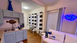 A compact living space with a kitchenette, a dining area, and a seating area with a neon shark decoration. - Salty Shark Q1 | Deck Patio (Galveston)