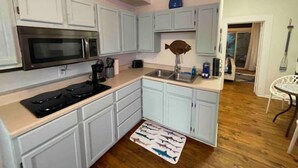 A kitchen with white cabinets, a microwave, a fish-shaped vase, and a wooden floor. - Salty Shark Q1 | Deck Patio (Galveston)