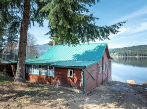 A cabin with a green roof, a wooden exterior, and a view of a lake.