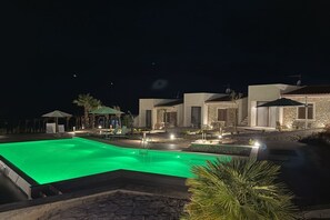 Ein Nachtblick auf ein Resort mit Schwimmbad, Steinbauten und Außenbereichen mit Sitzgelegenheiten.