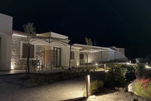 Un bâtiment en pierre doté d’une terrasse avec des parasols, d’un chemin en pierre et d’un petit jardin.