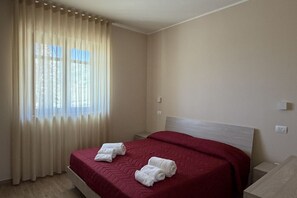 Une chambre d’hôtel avec un lit, une table de chevet, une fenêtre avec des rideaux et un interrupteur fixé au mur.