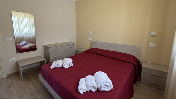 Hotellihuone, jossa on sänky, penkki, lipasto ja peili.