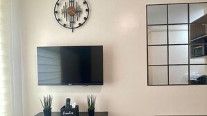 Ett modernt vardagsrum med en platt-TV, en dekorativ klocka, en liten växt och ett matbord.