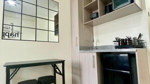 Ett kompakt kök med en inbyggd mikrovågsugn, ett svart kylskåp och ett litet matbord med två pallar.
