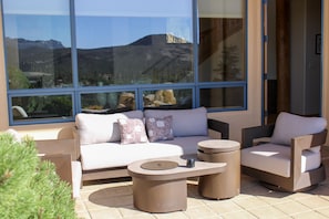 Un espacio al aire libre moderno con sofás, sillones y una mesa de centro, con vistas a un paisaje montañoso a través de amplios ventanales.