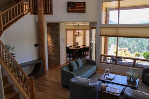 Amplia sala de estar con escalera, comedor y ventanas grandes con vistas al exterior.