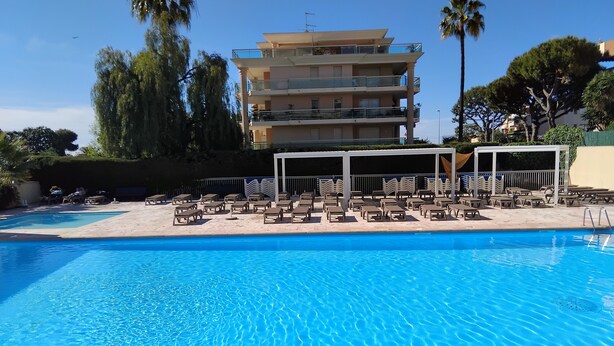 A swimming pool with lounge chairs and a covered area, surrounded by a multi-story building with balconies. - Sea and Sun (Saint-Laurent-du-Var)