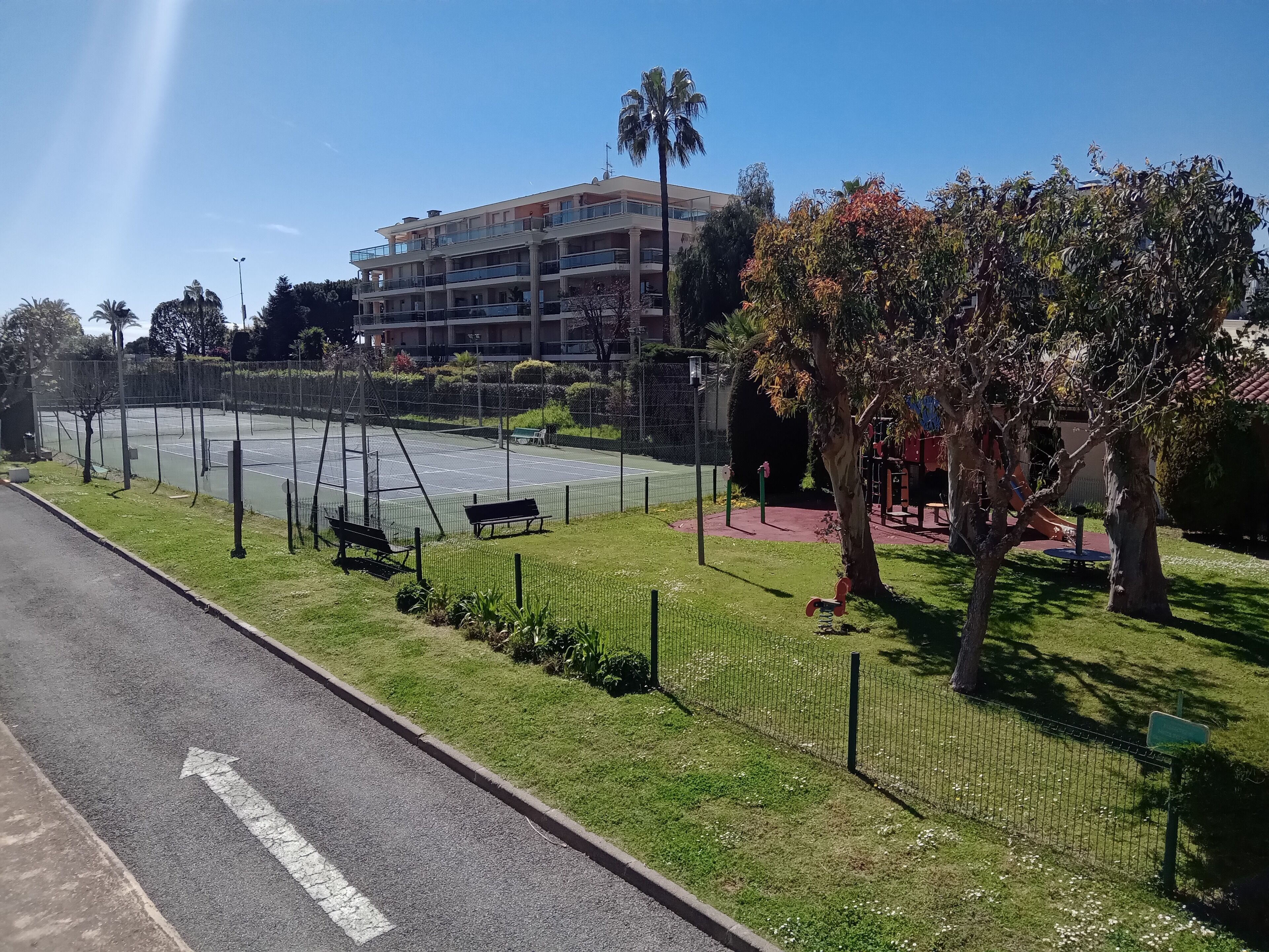 Een hotel met meerdere verdiepingen, balkons, een tennisbaan en een speeltuin.