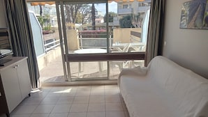 A room with a white sofa, a dining table, and a view of an outdoor balcony with plants and buildings. - Sea and Sun (Saint-Laurent-du-Var)