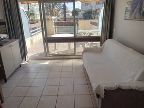 Ein Zimmer mit einem weißen Sofa, einem Esstisch und Blick auf einen Balkon mit Pflanzen und Gebäuden.
