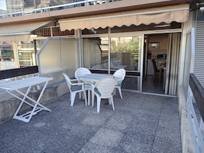 A balcony with a table and chairs, a small table with a striped tablecloth, and a view of a building with a balcony. - Sea and Sun (Saint-Laurent-du-Var)