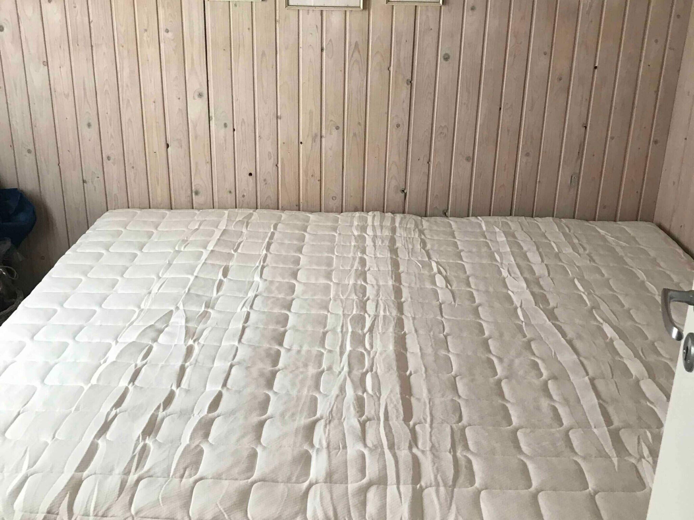 Une pièce avec un mur lambrissé en bois, un lit doté d’un matelas à texture particulière et une porte avec une poignée.