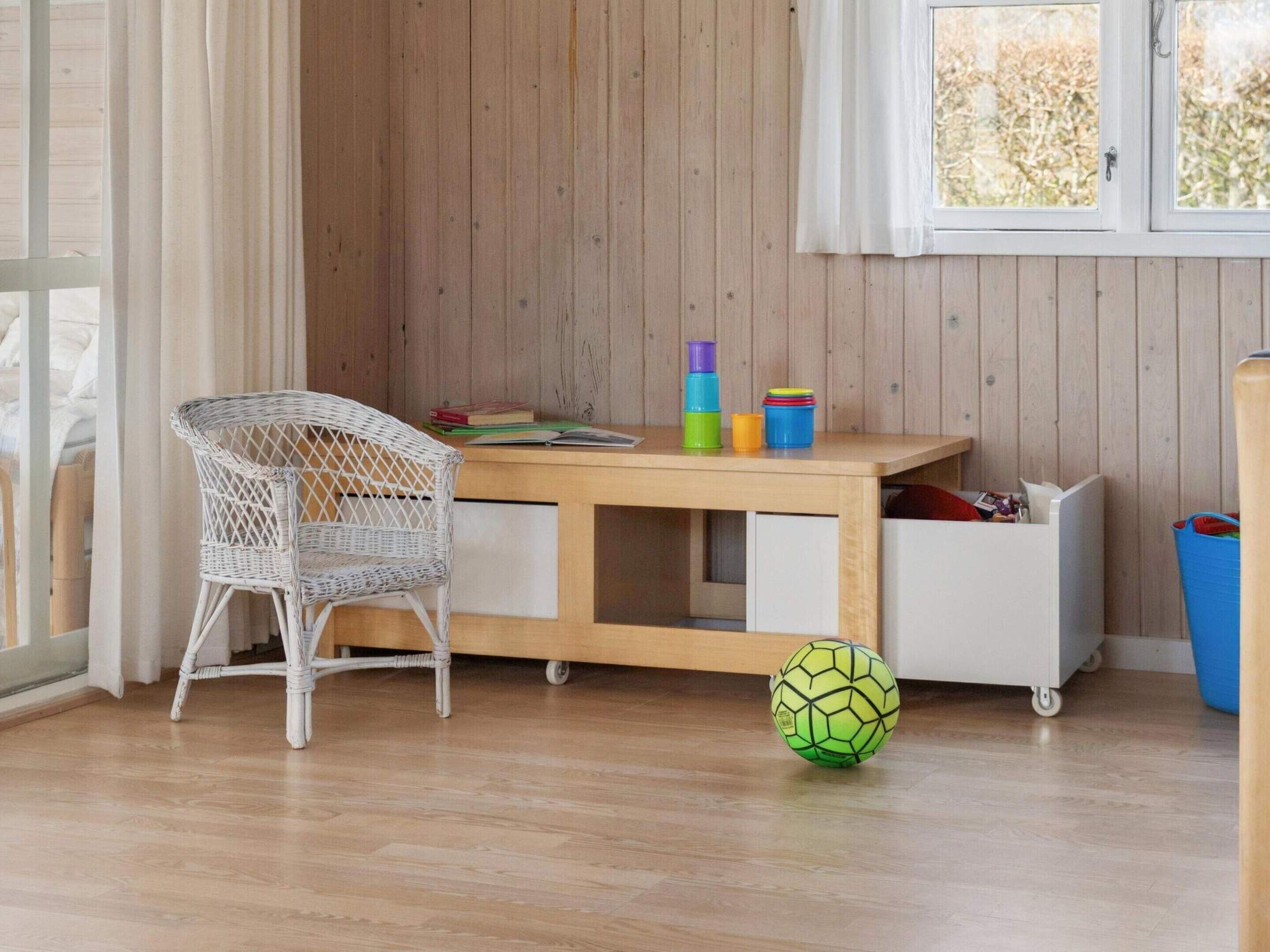 Une pièce avec un fauteuil en osier, un bureau en bois, un meuble de rangement blanc et un ballon de foot sur le sol.