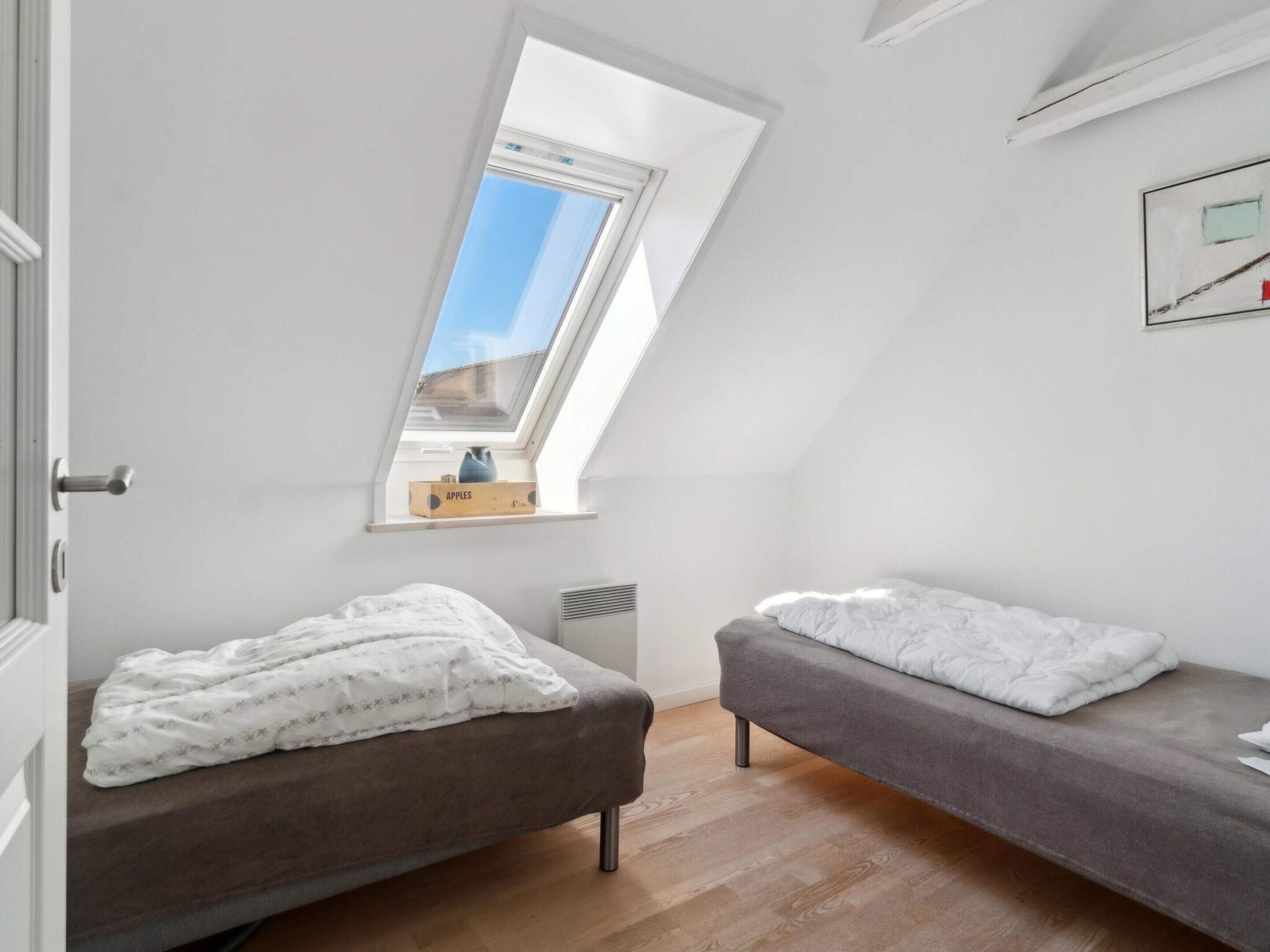Une petite chambre moderne avec deux lits, une lucarne et une fenêtre.