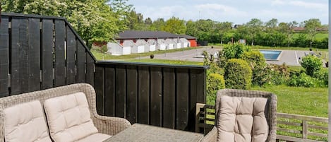 An outdoor patio with wicker furniture, a table, and a view of a swimming pool and buildings in the background.
