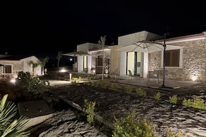 A nighttime view of a modern outdoor patio area with stone flooring, outdoor seating, and a well-lit entrance. - Sea-view apartment with a pool (Telegrafo)