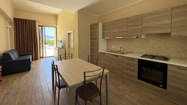 A modern kitchen with a dining area, wooden cabinets, and a view through the glass door. - Sea-view apartment with a pool (Telegrafo)