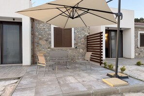 Un patio al aire libre con una mesa y sillas, un paraguas grande y un muro de piedra.