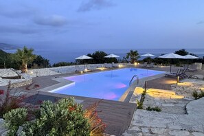 Una piscina con vistas al mar, rodeada de sillas y sombrillas de playa.