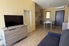 Ein modernes Wohnzimmer mit Flachbildfernseher, einer Couch, einem Essbereich mit Tisch und Stühlen, einer Küche mit Holzausstattung und einer Tür zu einem weiteren Raum.