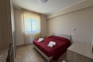 A hotel room with a bed, a wooden desk, a window with curtains, and a light-colored floor. - Sea-view apartment with a pool (Telegrafo)