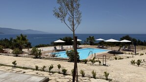 A pool area with lounge chairs and umbrellas, surrounded by small trees and a view of the sea. - Sea-view apartment with a pool (Telegrafo)